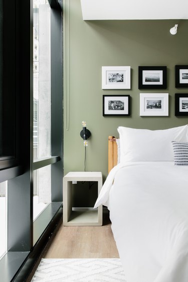Modern bedroom with green accent wall, black and white photos, nightstand, sconce, rug